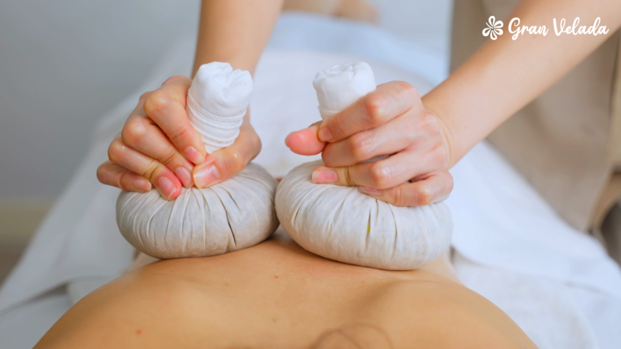 Aplicación de pindas relajantes calientes durante un masaje corporal sobre la espalda.