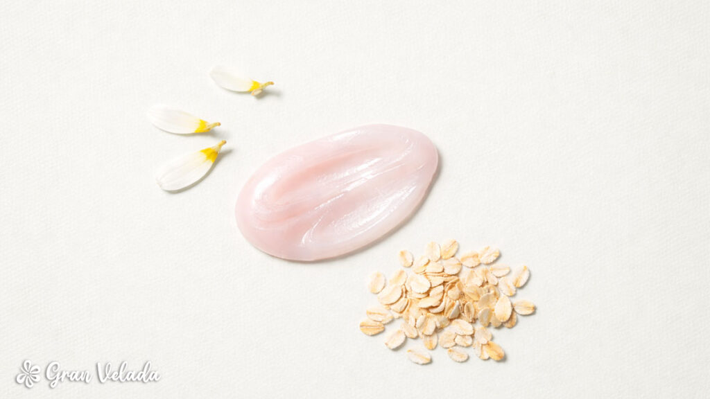 Amostra do sabonete rosa perolado, ao seu lado pétalas de flor de camomila e aveia.